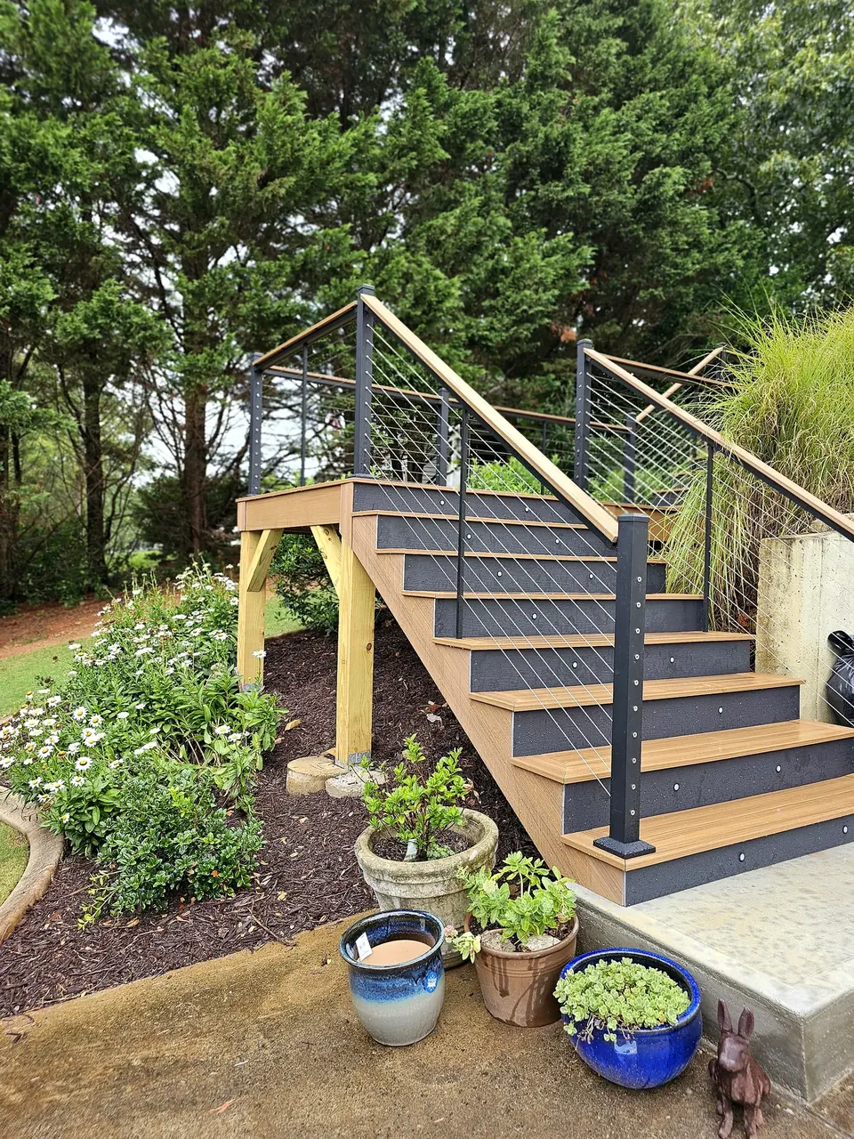 Exterior deck stairs with black metal railings beside garden plants
